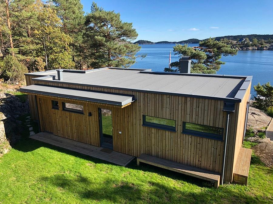 Anneks i ubehandlet tre med flatt tak på en gressplen ved sjøen