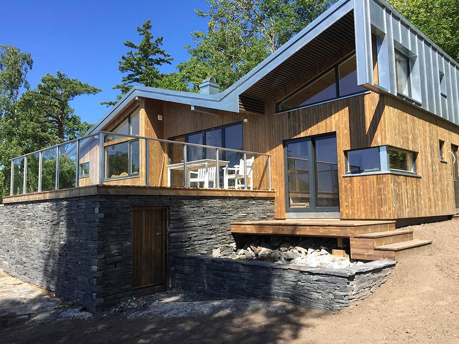 Moderne hytte i ubehandlet tre og skifer, med glassrekkverk på terrassen