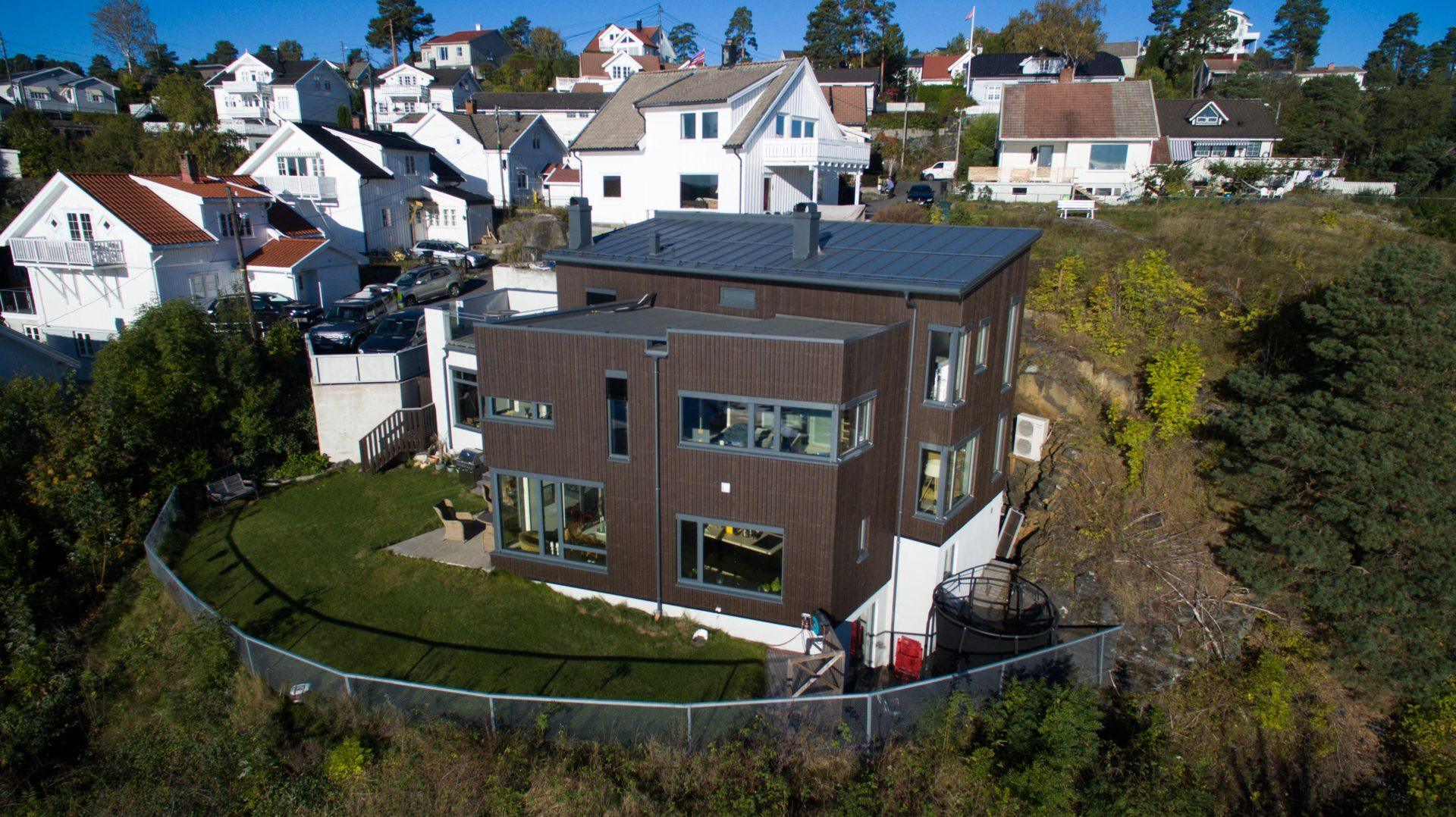 Brunt bolighus i tre etasjer med hage, midt i hvite trehus