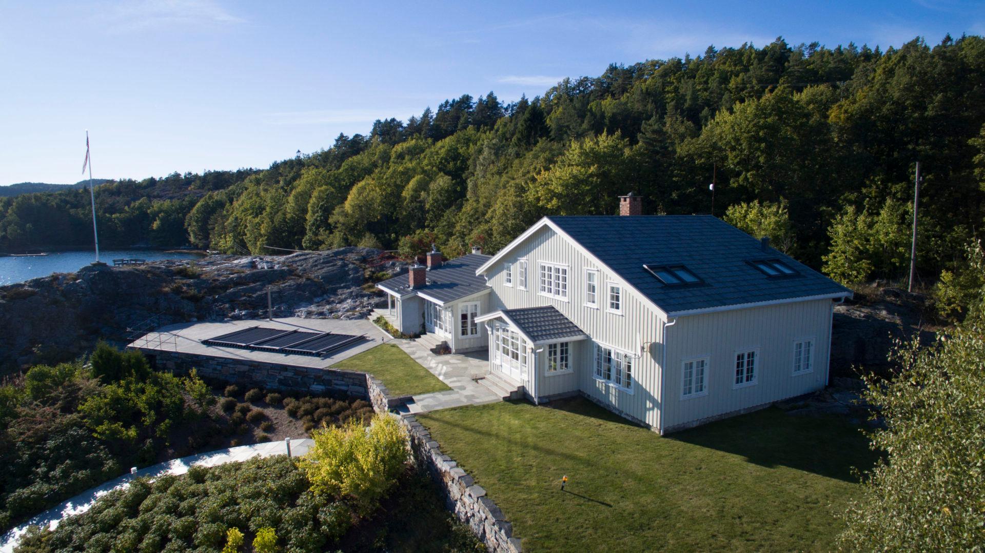 Hvitt hus med takterrasse ved sjøen, omgitt av skog
